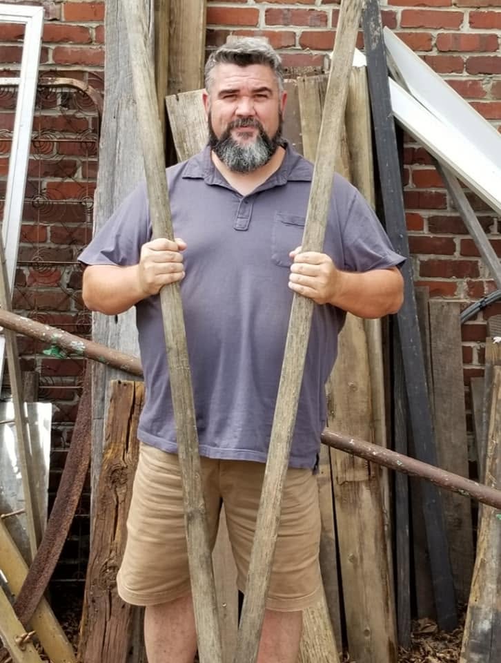 Tim Carmical carrying two long wooden boards through a work area