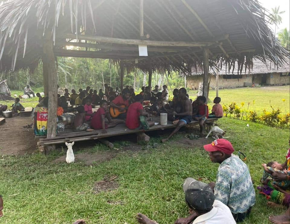 Adults and children gathered beneath a large open shelter in Papua New Guinea