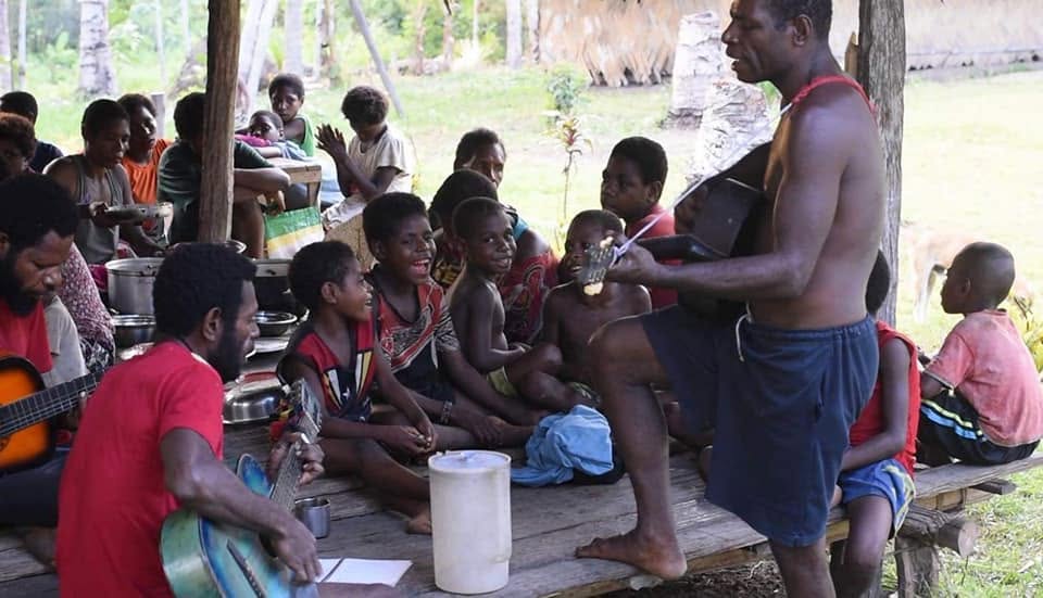 Adults and children gathered for music beneath an open shelter in Papua New Guinea
