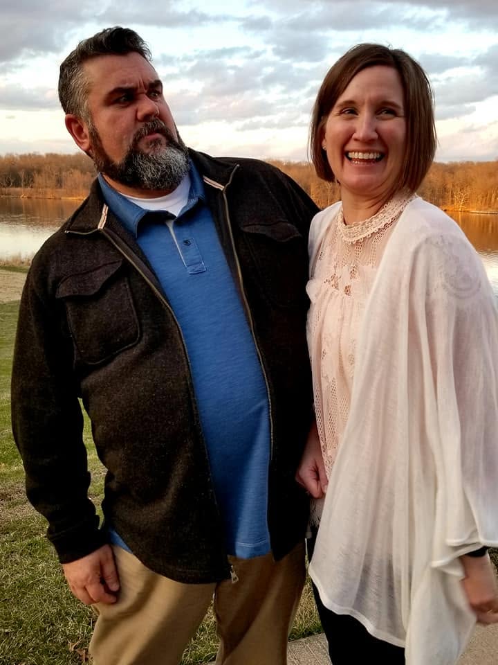 Tim Carmical looking sideways while Joan laughs beside a lake